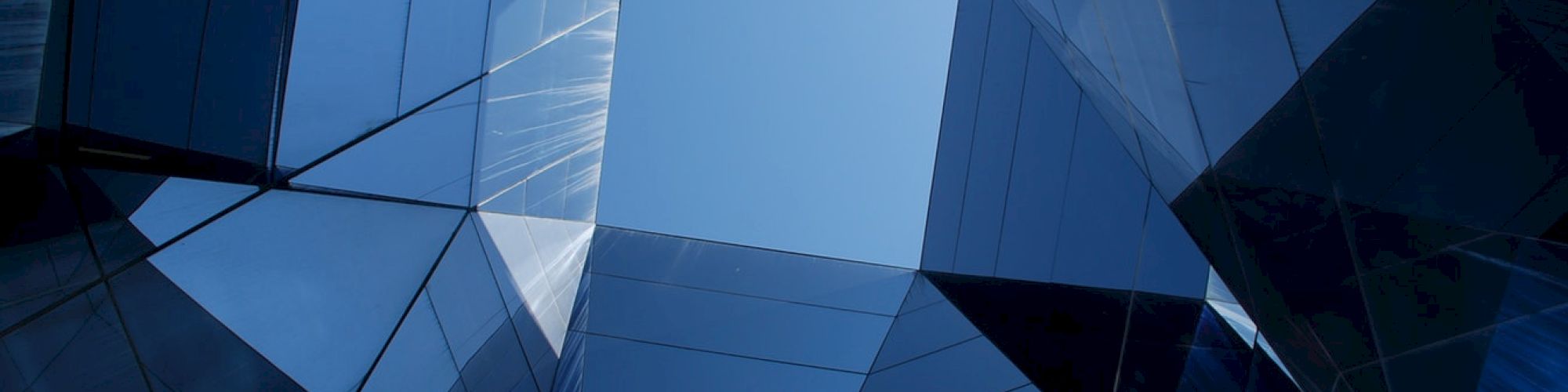 Geometric arrangement of glass buildings with reflections, framing a clear sky at the center of the composition.