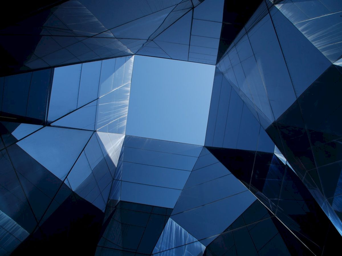 The image shows modern glass buildings forming a geometric pattern with a clear blue sky visible through the center.