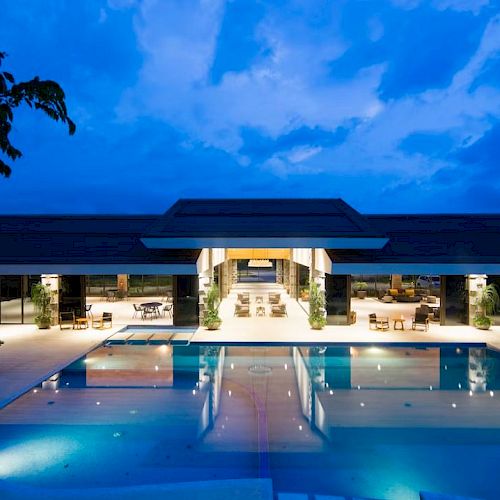 A luxurious outdoor pool area at dusk, with a modern building in the background, beautifully lit with seating and ambient lighting.