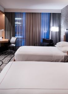 A modern hotel room with two beds, wall-mounted TV, desk, and patterned wallpaper.