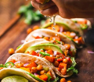 a hand squeezing lime juice over tacos