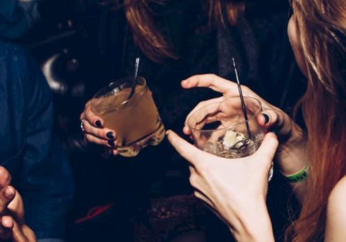 A group of people enjoying drinks at a lively social gathering, with laughter and animated conversation in a dimly lit setting.