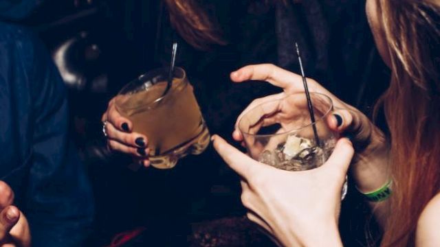 A group of people enjoying drinks at a lively social gathering, with laughter and animated conversation in a dimly lit setting.