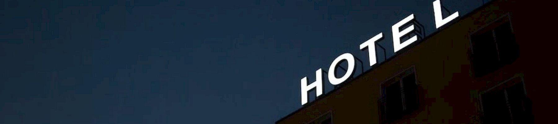 A building facade at night with a glowing "HOTEL" sign missing the letter "L," against a dark sky.