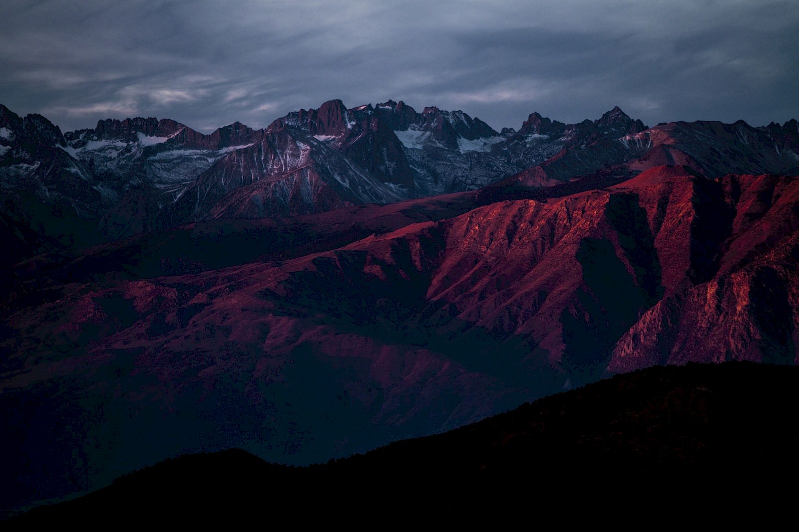 A mountain range with dramatic lighting and shadows beneath a cloudy sky, creating a striking and atmospheric landscape.