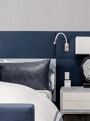 A modern bedroom with a blue upholstered headboard, a white and blue bed, and a nightstand with a lamp and decor.