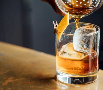 a cocktail is being strained into a glass with ice and an orange twist