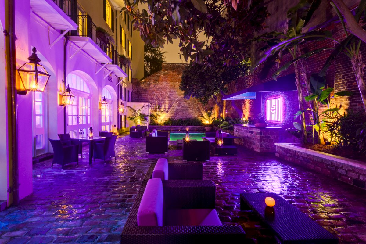 A nighttime view of a hotel courtyard with purple lighting, a pool, and outdoor seating.