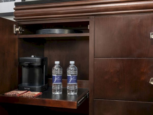 A cabinet with a coffee machine, two bottled waters, and coffee packets.