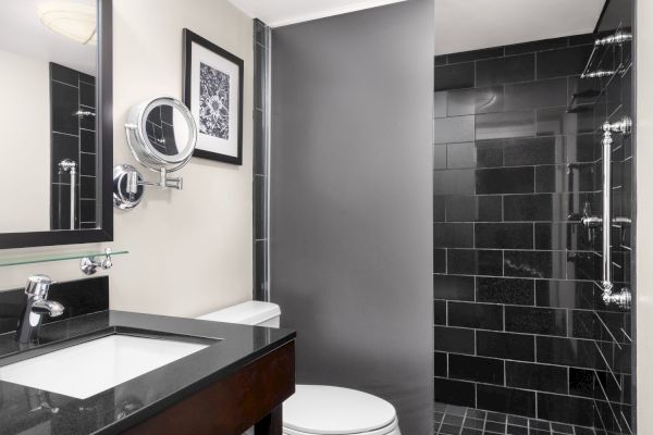 A modern bathroom with a black-tiled shower, sink with a mirror, and a framed picture on the wall.