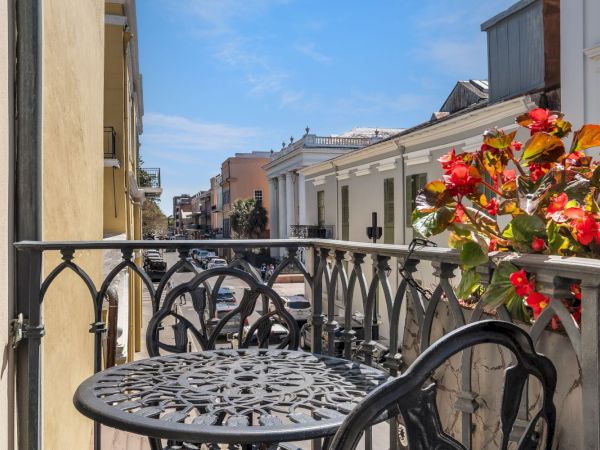 A balcony with decorative metal chairs and a table, overlooking a charming street with historic buildings and vibrant flowers.