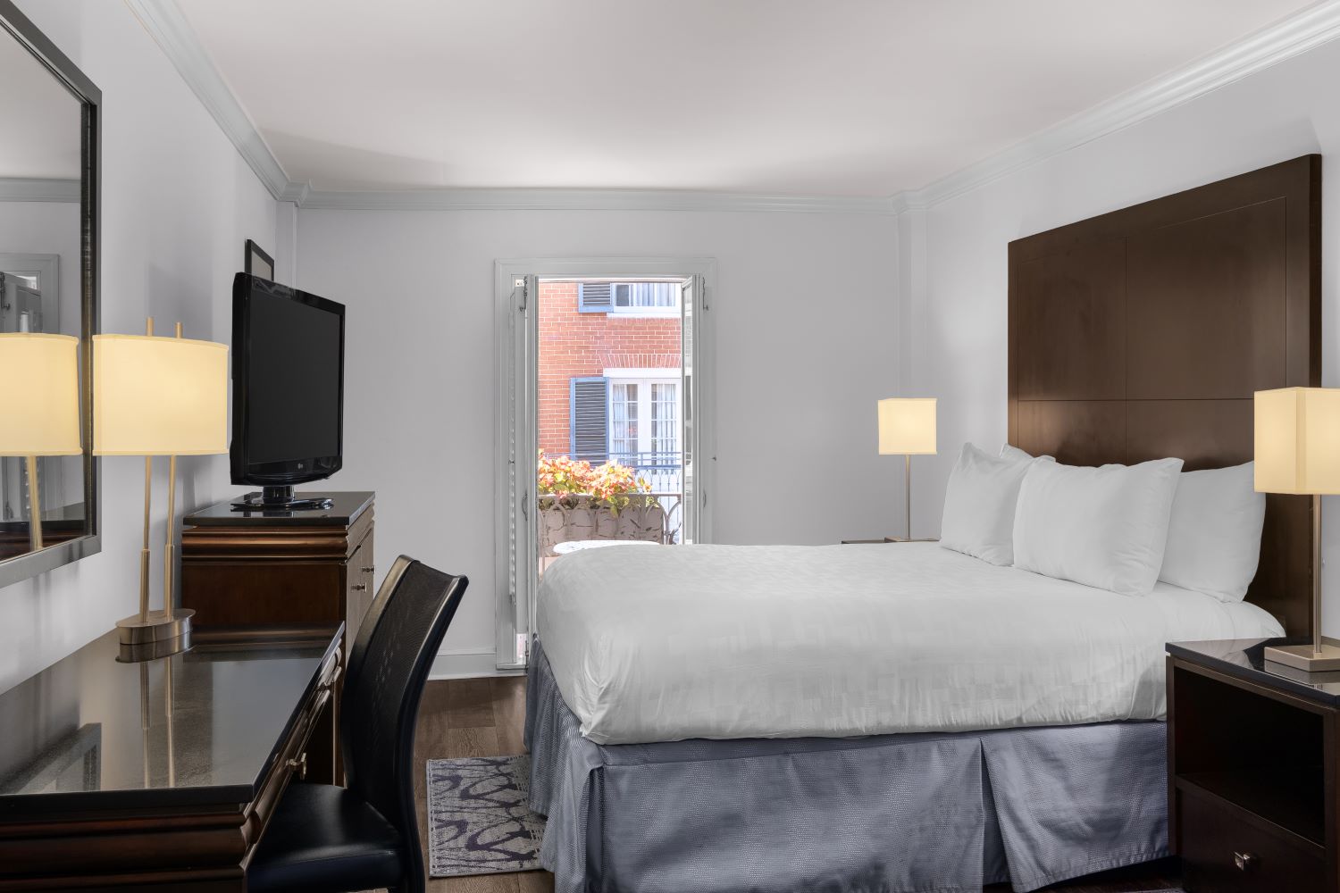 A hotel room with a large bed, desk, TV, and window