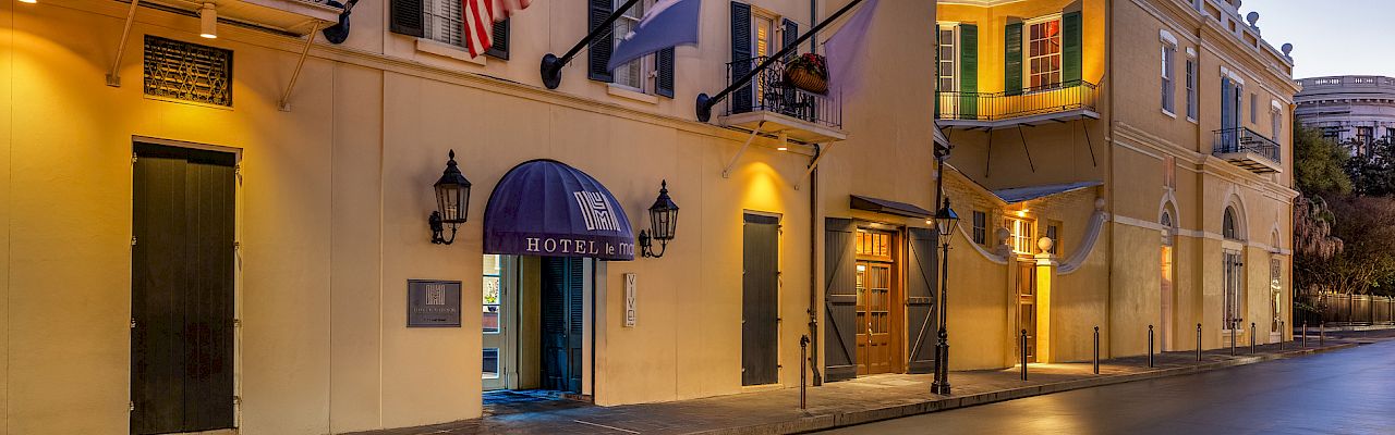 A beautifully lit hotel with flags outside, framed by charming architecture on a quiet street at dusk.