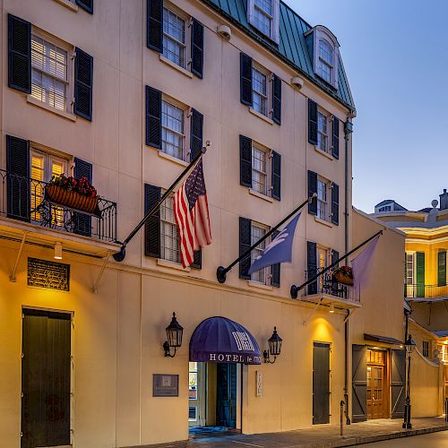 A beautifully lit hotel with flags outside, framed by charming architecture on a quiet street at dusk.