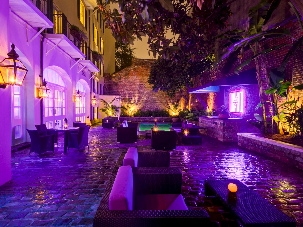 A dimly lit, vibrant outdoor courtyard with purple lighting, modern seating, and lush greenery.