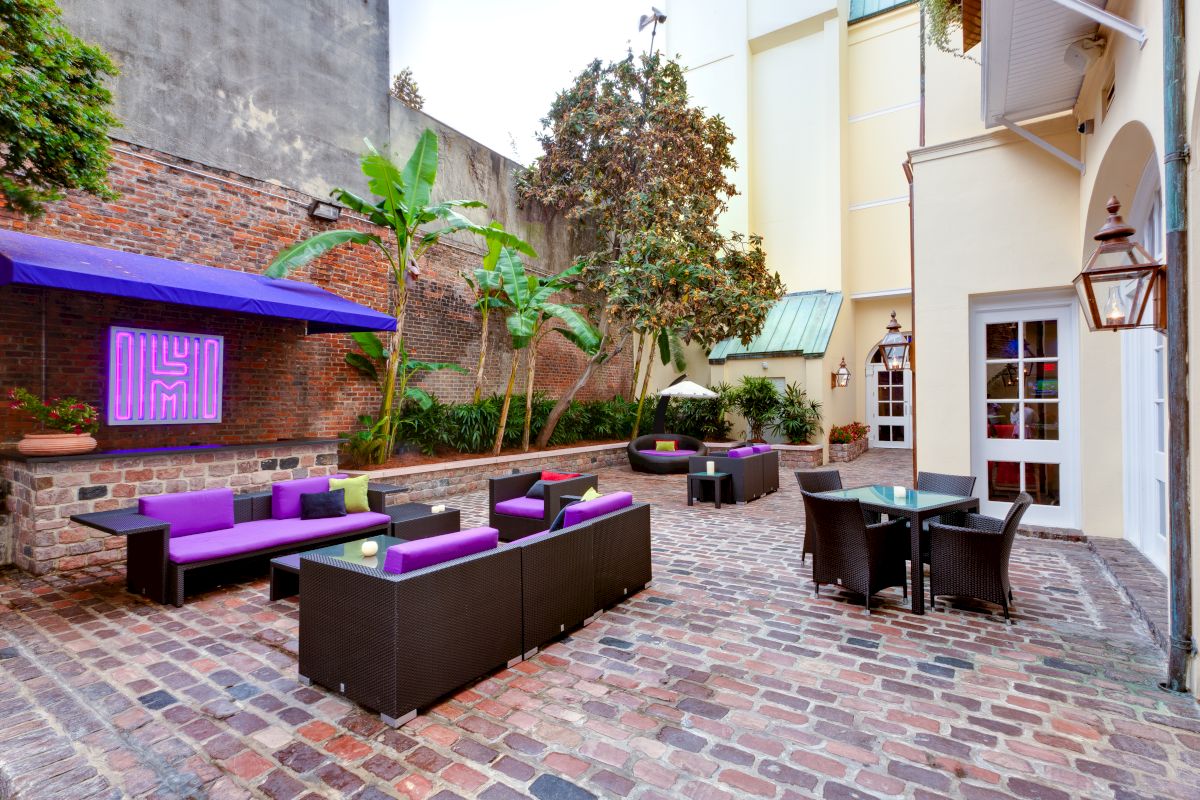 A cozy outdoor seating area with wicker furniture, purple accents, and brick pavers.