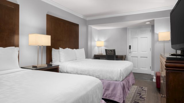 A hotel room with two beds, a desk, and a TV