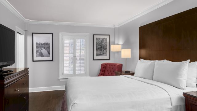 A wide view of a hotel room with a king-size bed, dresser, TV, chair, and lamp.