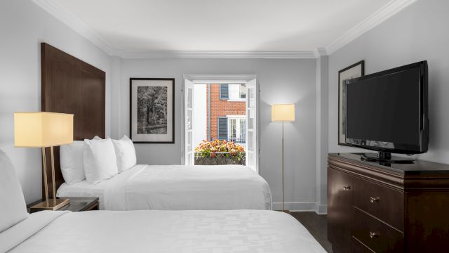 A hotel room with two beds, a TV, lamps, and a window with a view.