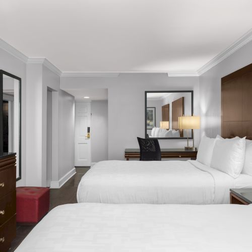The image shows a hotel room with two beds, a TV, a mirror, and bedside lamps on a wooden surface.
