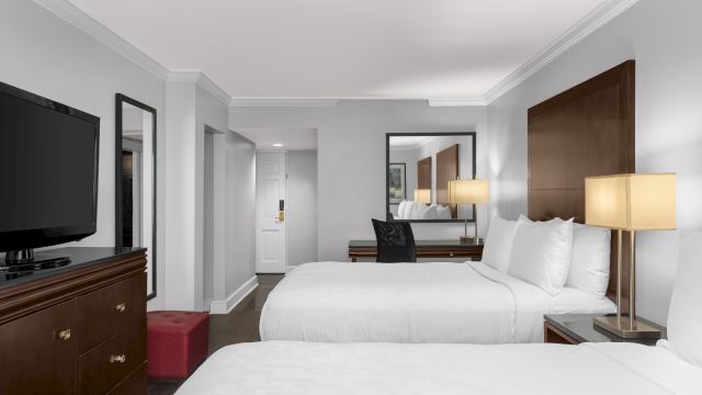 A hotel room with two beds, a flat screen TV on a dresser, and a lamp on a nightstand.
