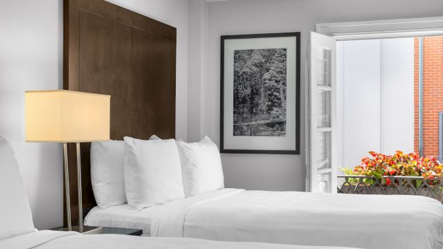 A wide view of a hotel room with a large bed, a lamp, and a window with flowers.