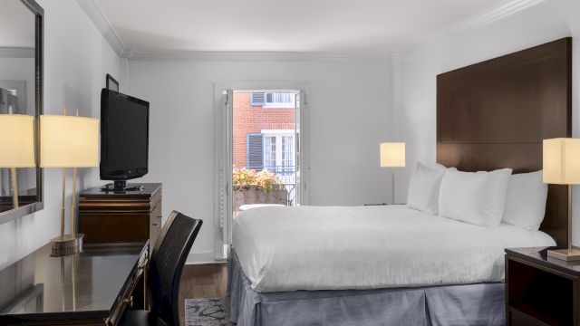 A wide view of a hotel room with a bed, desk, TV, and balcony.