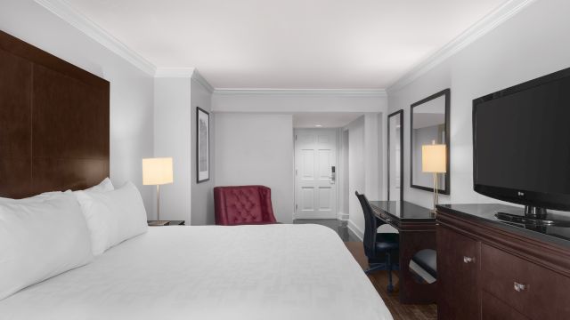 A wide view of a hotel room with a king-sized bed, desk, chair, and TV