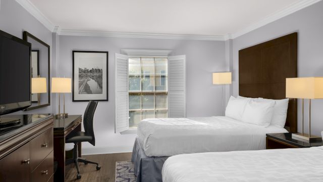 A hotel room with two beds, a desk, and a TV.