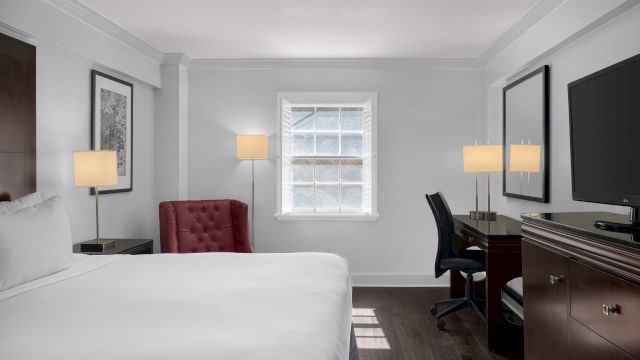 A wide view of a hotel room with a bed, desk, TV, and window