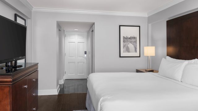 A wide view of a hotel room with a bed, TV, lamp, and artwork.