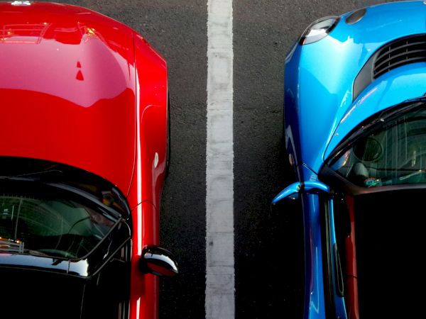 Aerial view of a red car and a blue car parked side by side, separated by a white line on a dark pavement.