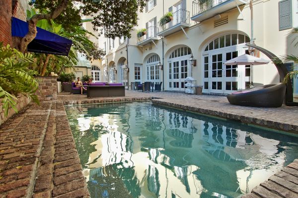 A courtyard features a small pool, seating area, and lush greenery, set against buildings with tall windows and balconies.