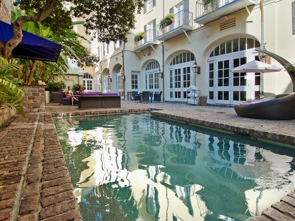 A courtyard features a small pool, seating area, and lush greenery, set against buildings with tall windows and balconies.