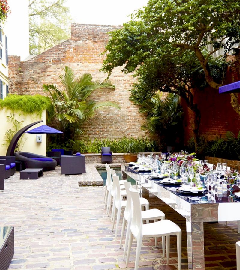 A long table set for dining in an outdoor courtyard with a brick wall and landscaping.