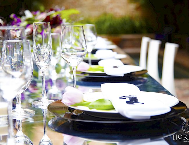 A long dining table is elegantly set with plates, wine glasses, and napkins, with floral decorations.
