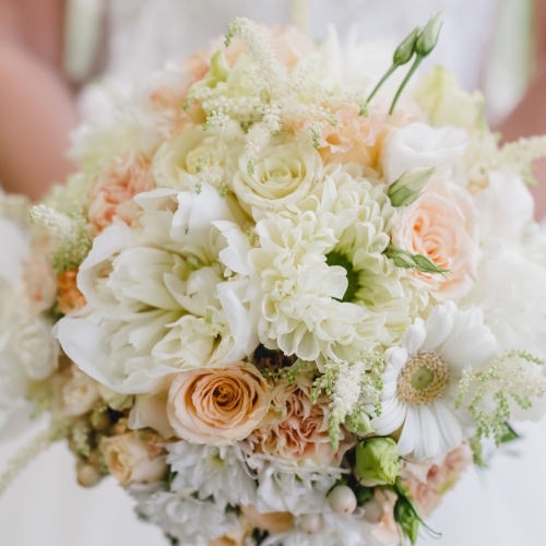 Pastel floral bouquet of white roses, peonies, and greenery with soft peach accents.