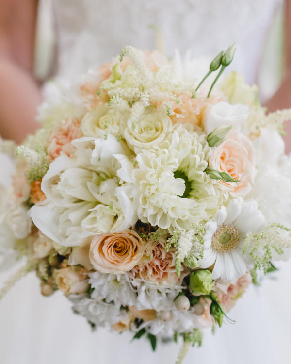 Pastel floral bouquet of white roses, peonies, and greenery with soft peach accents.