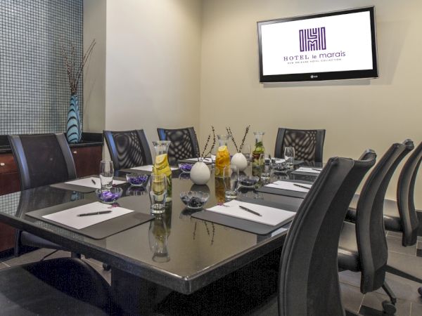A modern conference room with a glass table, chairs, notepads, and a screen displaying a logo, arranged for a meeting.