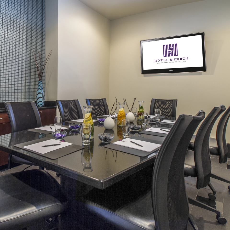 A well-equipped meeting room with a long table, chairs, and a screen on the wall.