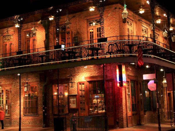 A dimly lit two-story brick building with balconies, street lamps, and hanging lanterns, reminiscent of a historic or colonial-style corner pub or restaurant.