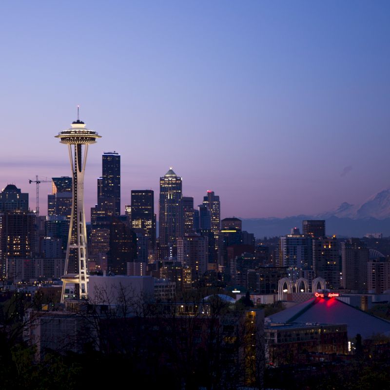 A city skyline with the Space Needle, skyscrapers, and a mountain in the background during twilight in Seattle.