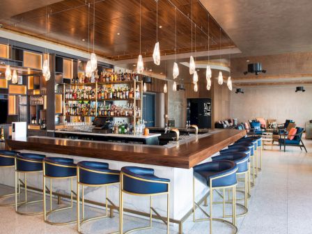A modern bar with high stools, pendant lights, and a well-stocked liquor shelf, featuring a sleek interior design and seating area.