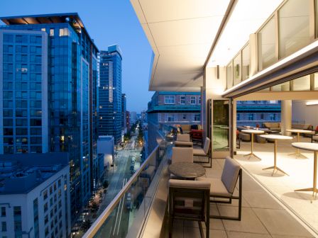 A modern rooftop terrace with seating overlooks a cityscape with tall buildings, seen during the evening.