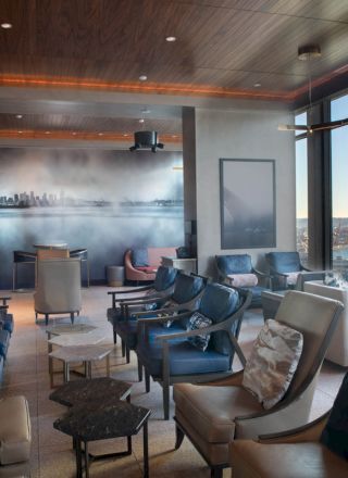 A modern lounge with elegant seating, large windows displaying a waterfront view, and a wall art piece depicting a city skyline.