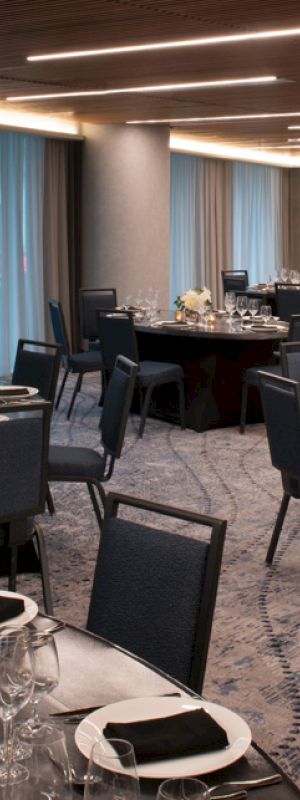 The image shows an elegant banquet hall with round tables set for dining, featuring dark chairs, neatly arranged table settings, and floral centerpieces.
