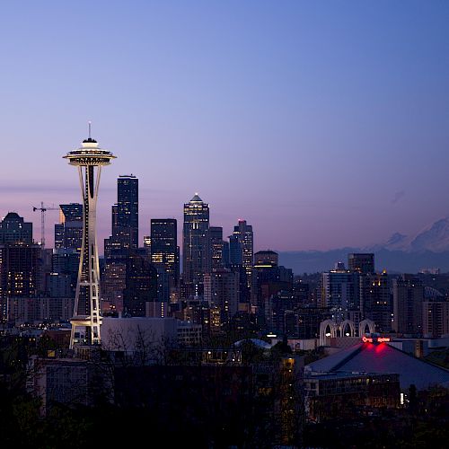 Seattle skyline at dusk with the iconic Space Needle and Mount Rainier in the background under a twilight sky.